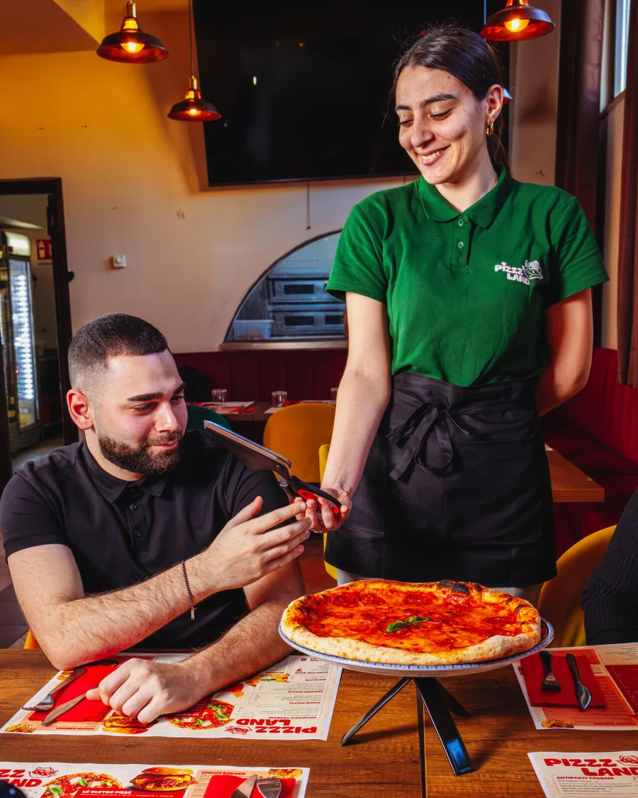 Cameriera Pizzzland sorridente consegna le forbici taglia-pizza a un cliente al tavolo